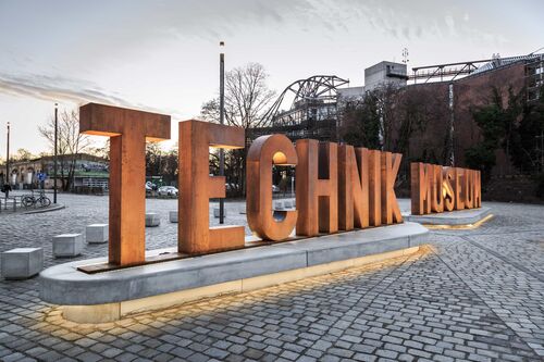 A bronze sculpture of the letters ‘Technik Museum’ stands in front of the building of the same museum.