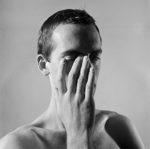 Black-and-white photograph by Peter Hujar: The upper body of a naked person is visible in the frame. A hand rests on the person’s neck, whilst the shoulders and chest are clearly defined. The background is neutral and evenly lit, which strongly emphasises the body and the lines of the pose.