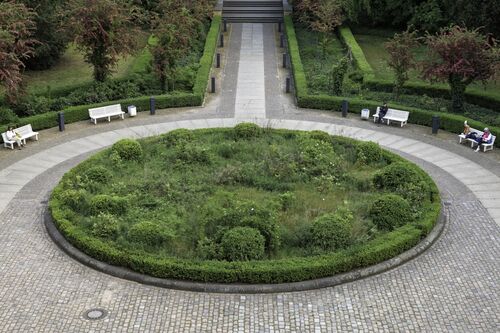 Das grasbewachsene Rondell Das Recht auf Faulheit des Künstlers John Knight vor dem Hamburger Bahnhof, das mit verschiedenen Gräsern und Sträuchern bewachsen ist und von einem Steinweg mit Bänken umfasst wird