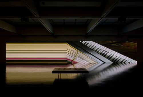 Großformatige Videoinstallation mit Klaviertasten und Flügelmechanik in einem abgedunkelten Ausstellungsraum.
