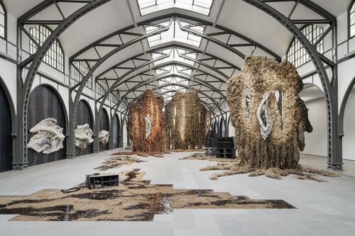 Rauminstallation von Klára Hosnedlová: Organisch geformte, turmartige Skulpturen aus braunen, baum- oder mineralartigen Materialien stehen in einem hell beleuchteten Raum
