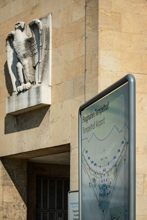 Historisches Gebäude des Flughafens Tempelhof mit einem Adlerrelief und einem aktuellen Flughafenplan im Vordergund.