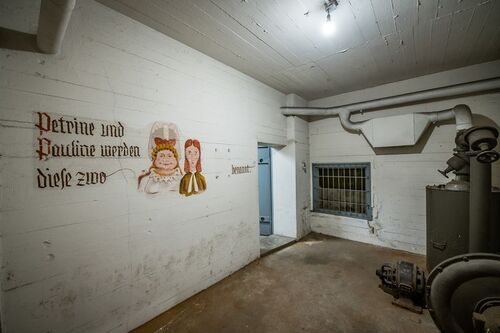 Blick in einen Luftschutzbunker im Flughafen Tempelhof. An der Wand ist eine Zeichnung und ein Zitat von Wilhelm Busch zu sehen.