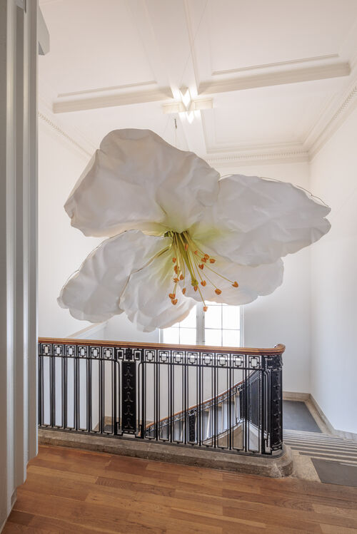 Eine große weiße Blüte im Treppenhaus des Hamburger Bahnhofs, die von der Decke hängt.