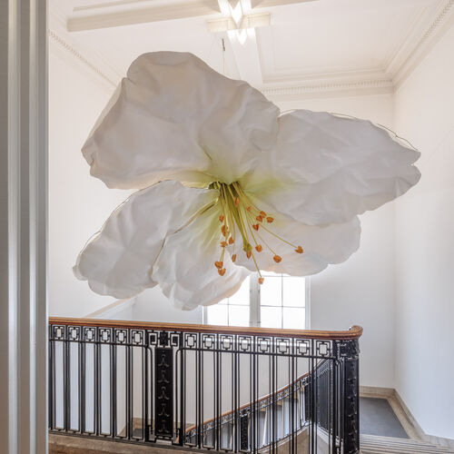 Eine große weiße Blüte im Treppenhaus des Hamburger Bahnhofs, die von der Decke hängt.