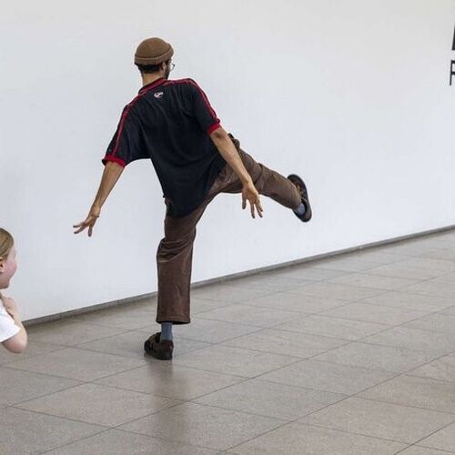 Eine männliche Person läuft auf einer freien Fläche im Museum mit großen Schritten und ist von Kindern umringt, die versuchen mit viel körperlicher Leidenschaft und großer Heiterkeit zu folgen