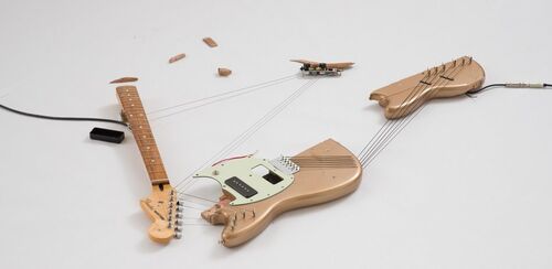 Detail der Ausstellung Naama Tsabar. Ein auf weißem Boden liegendes zerstörtes hellbraunes Saiteninstrument, dessen Holzteile durch die Saiten noch verbunden sind.