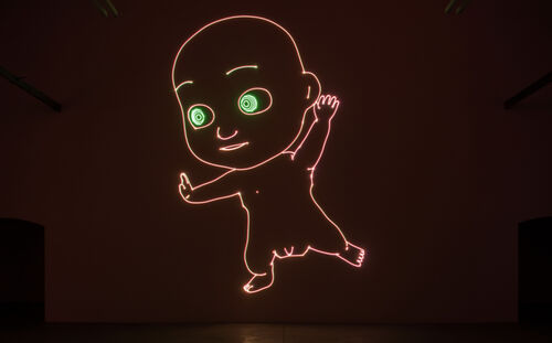 Eine bildfüllende Laserprojektion eines riesigen Babys in neonfarbenen Konturen und großen, grünen Augen vor dunkelbraunem Hintergrund von Matt Copson in der Installation Age of Coming