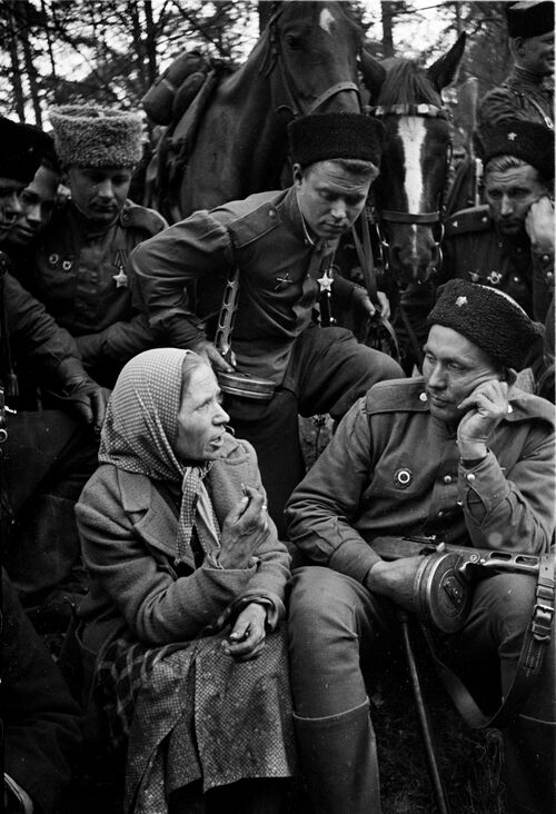 Das Schwarz-Weiß-Foto im Hochformat zeigt eine sitzende Frau, eine befreite sogenannte Ostarbeiterin, links im Vordergrund. Sie spricht zu einem ebenfalls sitzenden Soldaten, rechts im Vordergrund, der neben ihr sitzt. Sie trägt ein Kopftuch und einen Mantel. Ihr Kopf ist ihrem Gegenüber zugewendet. Beim Reden gestikuliert sie mit der rechten Hand. Ihren rechten Arm stützt sie auf ihren Schoß. Ihr linker Arm ruht auf ihrem linken Knie. Ihre Stirn ist leicht gerunzelt. Der sowjetische Soldat, zu dem sie spricht, stützt seinen Kopf auf seine linke Hand und sieht sie an. In seiner rechten Hand hält er eine sowjetische Maschinenpistole (Pistolet-Pulemjot Schpagina), dessen Lauf rechts aus dem Foto hinausweist. Er trägt eine Uniform, Stiefel und auf dem Kopf eine Pelzmütze. Im Hintergrund sind in der oberen Bildhälfte sechs weitere dicht beieinander Soldaten zu sehen. Ihre Blicke sind alle auf die beiden sitzenden Personen im Vordergrund gerichtet. Auch zwei der Soldaten runzeln die Stirn. Der Soldat in der Mitte hält eine Leine. Hinter ihm stehen zwei eingespannte Pferde, deren Köpfe etwas zwischen die Soldaten hineinragen. Im Hintergrund stehen Bäume mit wenigen Blättern