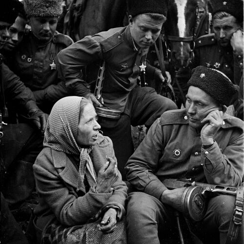 Das Schwarz-Weiß-Foto im Hochformat zeigt eine sitzende Frau, eine befreite sogenannte Ostarbeiterin, links im Vordergrund. Sie spricht zu einem ebenfalls sitzenden Soldaten, rechts im Vordergrund, der neben ihr sitzt. Sie trägt ein Kopftuch und einen Mantel. Ihr Kopf ist ihrem Gegenüber zugewendet. Beim Reden gestikuliert sie mit der rechten Hand. Ihren rechten Arm stützt sie auf ihren Schoß. Ihr linker Arm ruht auf ihrem linken Knie. Ihre Stirn ist leicht gerunzelt. Der sowjetische Soldat, zu dem sie spricht, stützt seinen Kopf auf seine linke Hand und sieht sie an. In seiner rechten Hand hält er eine sowjetische Maschinenpistole (Pistolet-Pulemjot Schpagina), dessen Lauf rechts aus dem Foto hinausweist. Er trägt eine Uniform, Stiefel und auf dem Kopf eine Pelzmütze. Im Hintergrund sind in der oberen Bildhälfte sechs weitere dicht beieinander Soldaten zu sehen. Ihre Blicke sind alle auf die beiden sitzenden Personen im Vordergrund gerichtet. Auch zwei der Soldaten runzeln die Stirn. Der Soldat in der Mitte hält eine Leine. Hinter ihm stehen zwei eingespannte Pferde, deren Köpfe etwas zwischen die Soldaten hineinragen. Im Hintergrund stehen Bäume mit wenigen Blättern