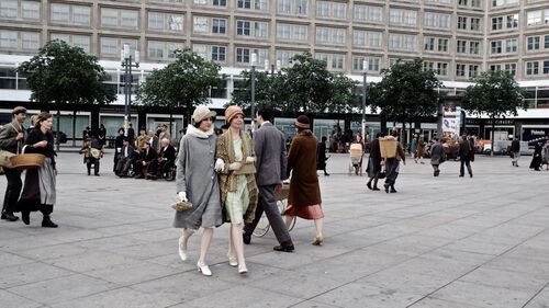 Auf den Alexanderplatz kommen zwei Frauen in historischer Kleidung aus dem Anfang des 20. Jahrhunderts in Richtung des Bildausschnitts. Ein Mann und eine Frau in ähnlichen Kostümen gehen in die entgegengerichtete Richtung.