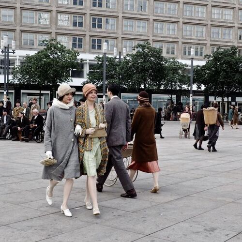 Auf den Alexanderplatz kommen zwei Frauen in historischer Kleidung aus dem Anfang des 20. Jahrhunderts in Richtung des Bildausschnitts. Ein Mann und eine Frau in ähnlichen Kostümen gehen in die entgegengerichtete Richtung.