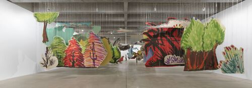 Die Installationsansicht Very volcanic over this green feather von Petrit Halilaj zeigt in einer weiträumigen Halle in den Raum gestaffelte großformatige Bilder in kräftigen Farben von Pflanzen und Tieren, wobei die Motive ausgeschnitten und wie in einem Theaterprospekt angeordnet sind