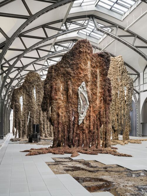 Rauminstallation von Klára Hosnedlová: Organisch geformte, turmartige Skulpturen aus braunen, baum- oder mineralartigen Materialien stehen in einem hell beleuchteten Raum