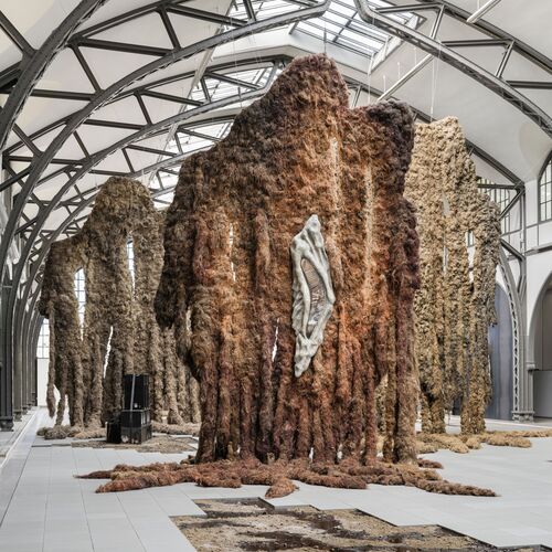 Rauminstallation von Klára Hosnedlová: Organisch geformte, turmartige Skulpturen aus braunen, baum- oder mineralartigen Materialien stehen in einem hell beleuchteten Raum